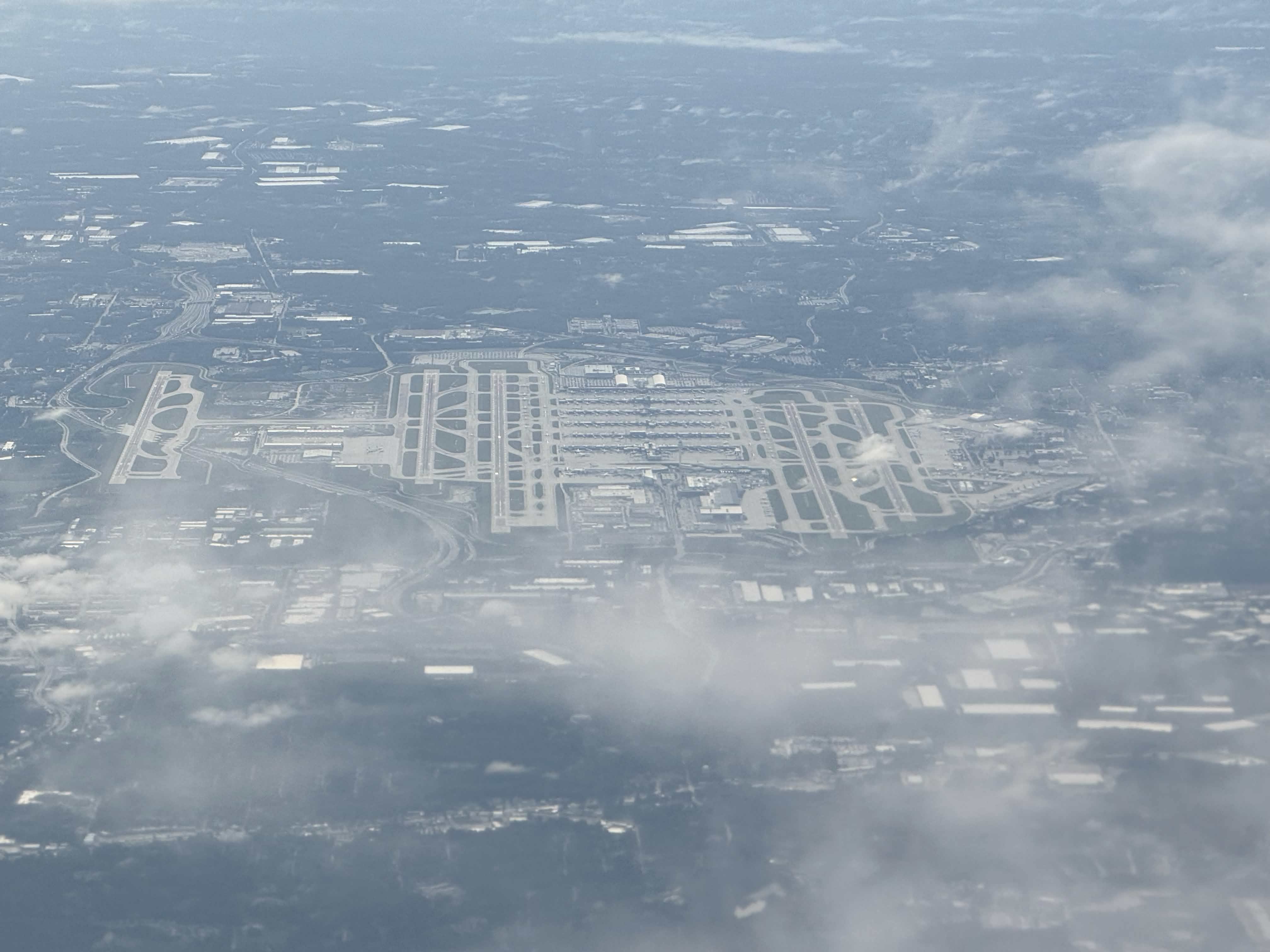 Aerial photograph over the Hartsfield-Jackson airfield in May 2026, taken from an aircraft window, with runways, taxiways and terminal buildings visible below; individual concourses are not distinguishable