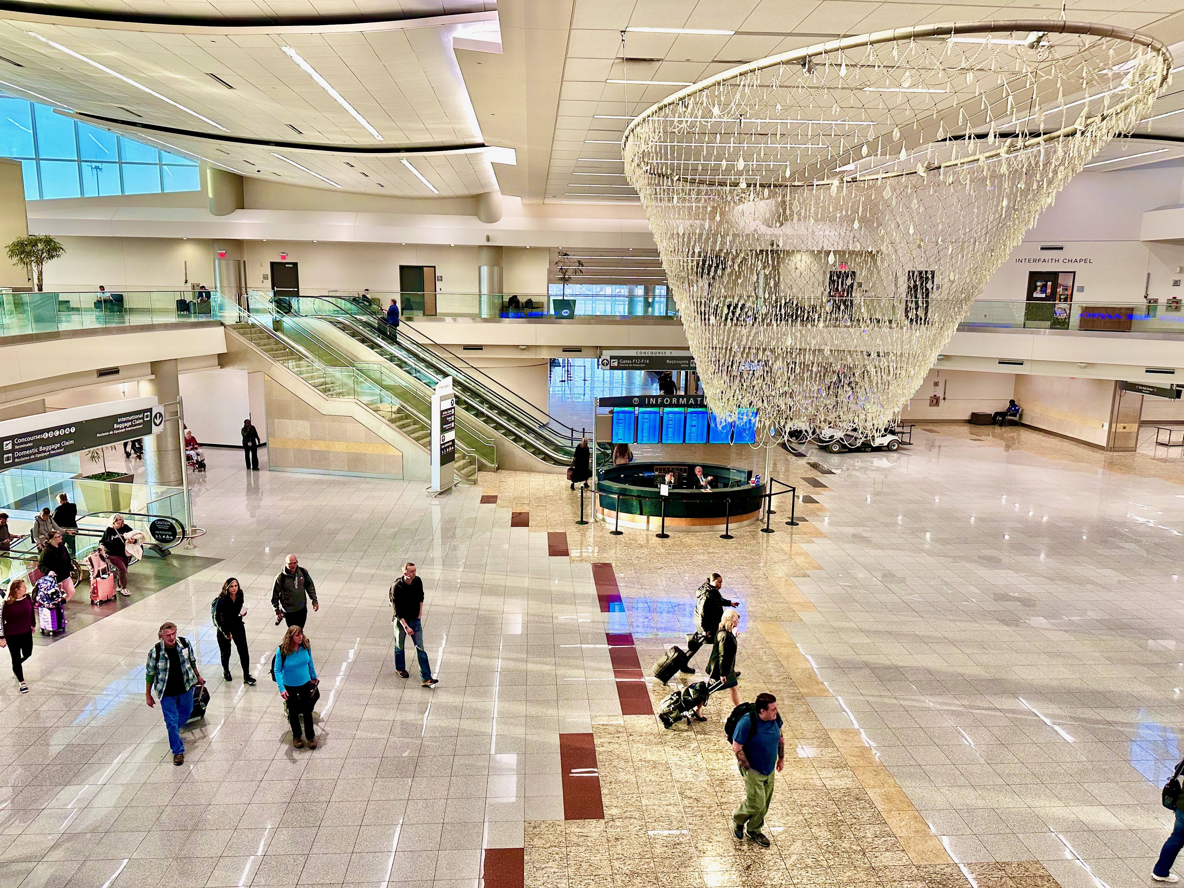 Interior photograph of the Concourse F central atrium in May 2023, a tall multi-level hall with a skylight, escalators and concession frontages around the floor