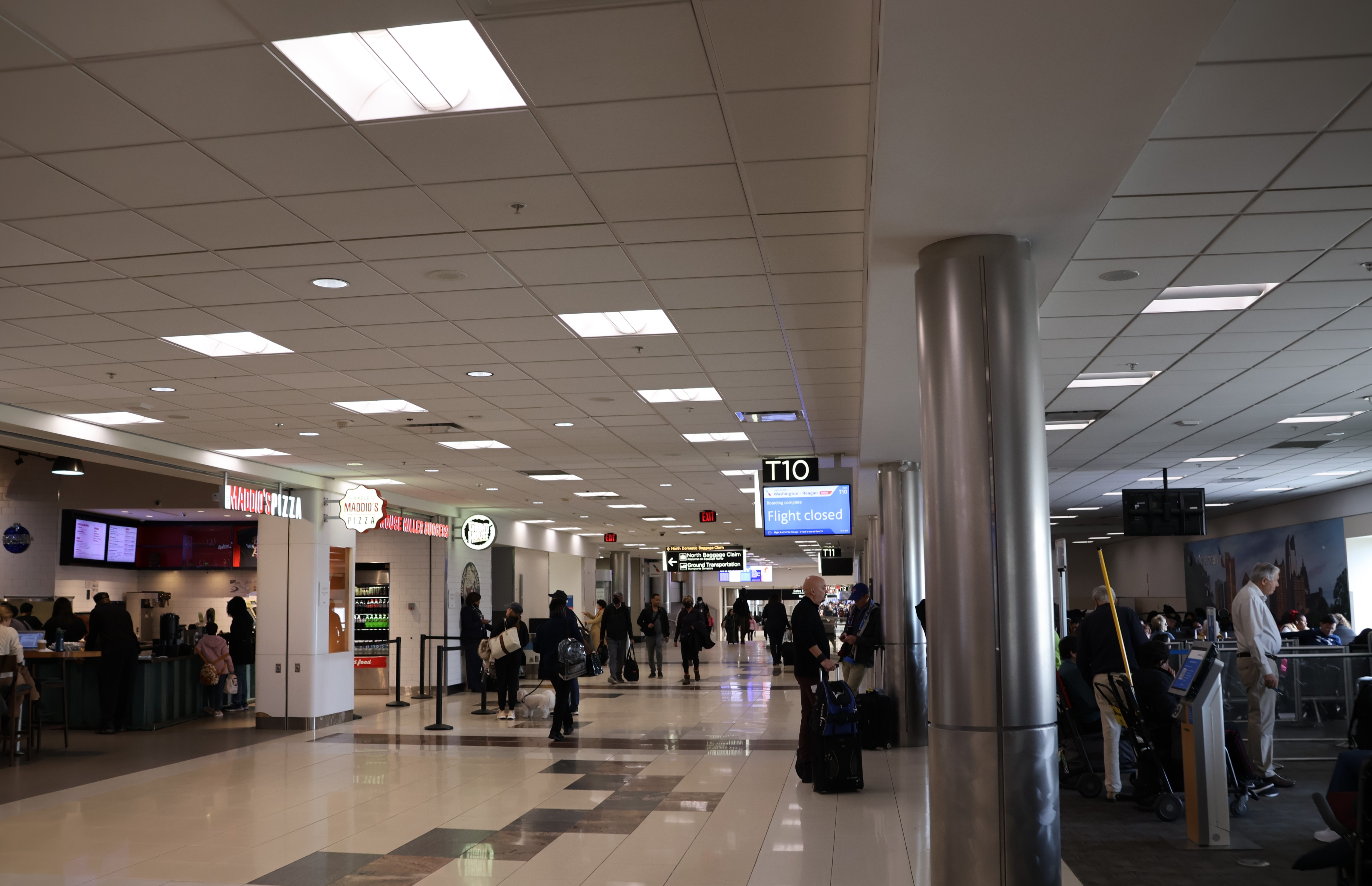 Interior photograph of the Concourse T corridor at gate T10 in December 2023, with gate seating, overhead signage and the corridor running toward the concourse end